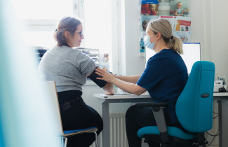 Terveydenhoitaja mittaa asiakkaalta verenpaineen.