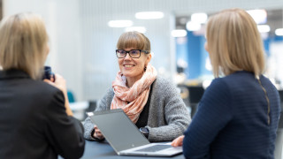Kolme henkilöä keskustelevat tietokoneiden ääressä. Kolme henkilöä keskustelevat tietokoneiden ääressä.