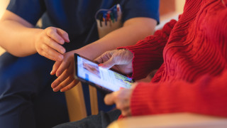 Kotihoidon ammattilainen näyttää ikäääntyneelle miten käytetään etähoivan tablettia. Kotihoidon ammattilainen näyttää ikäääntyneelle miten käytetään etähoivan tablettia.