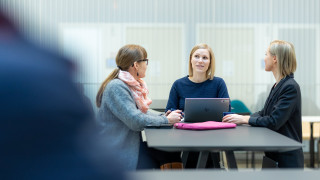 Kolme henkilöä istuvat pöydä ääressä. Kolme henkilöä istuvat pöydä ääressä.