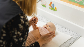 Vauva neuvolassa hoitopöydällä katselee terveydenhoitajaa. Vauva neuvolassa hoitopöydällä katselee terveydenhoitajaa.